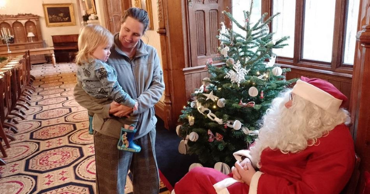 woman holding child stands in front of Father Christmas at Ushaw Historic House.